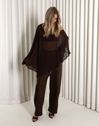 Woman wearing a dark brown outfit with sheer panels against a white curtain background