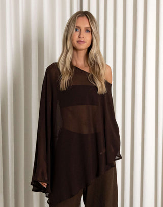 Woman wearing a dark brown outfit with sheer panels against a white curtain background