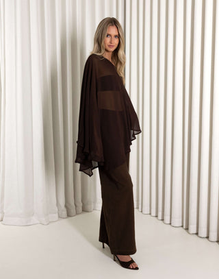 Woman wearing a dark brown outfit with sheer panels against a white curtain background