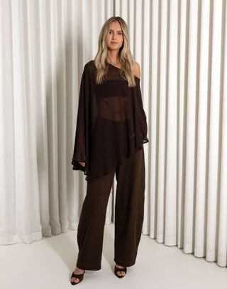 Woman wearing a dark brown outfit with sheer panels against a white curtain background