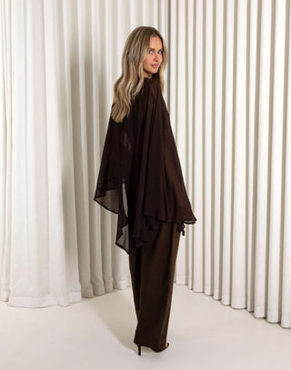 Woman wearing a dark brown outfit with sheer panels against a white curtain background