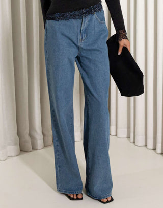 Person wearing blue jeans holding a black clutch against a neutral background