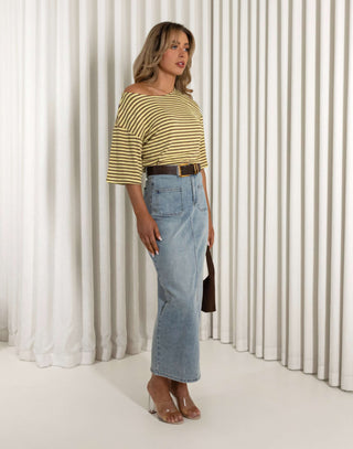 Woman wearing a striped yellow and green top and blue jeans standing against a white curtain. Martin stripe versatile off shoulder long length top