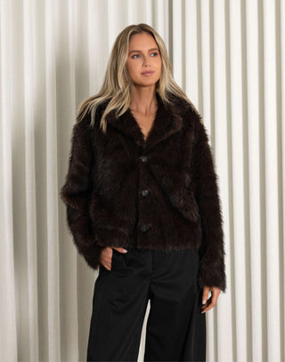 Woman wearing a dark brown faux fur jacket against a neutral background