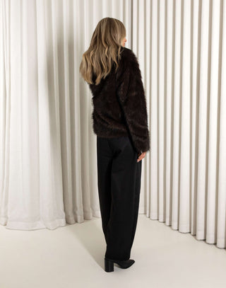Person wearing a dark fur coat standing in front of white curtains