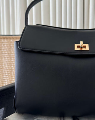 Black handbag with a gold clasp on a neutral background