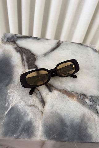 Black cat-eye sunglasses with brown tinted lenses resting on a gray and white marble surface.