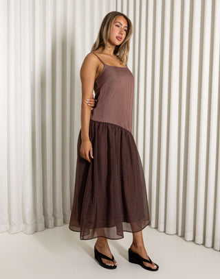 Woman wearing a brown dress standing against a white curtain. Nancy brown relaxed midi dress with adjustable straps
