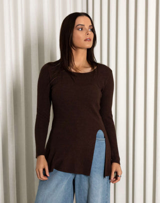 Woman wearing a brown top and blue jeans standing against a white curtain background