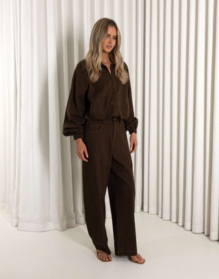 Woman wearing a brown outfit standing against a white curtain background