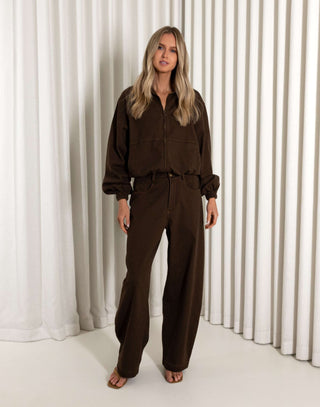 Woman wearing a brown outfit standing against a white curtain background
