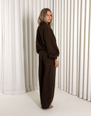 Woman wearing a brown outfit standing against a white curtain background