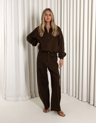 Woman wearing a brown outfit standing against a white curtain background