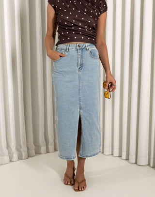 Woman wearing a polka dot top and denim skirt against a white curtain background Light denim high waisted skirt with front split