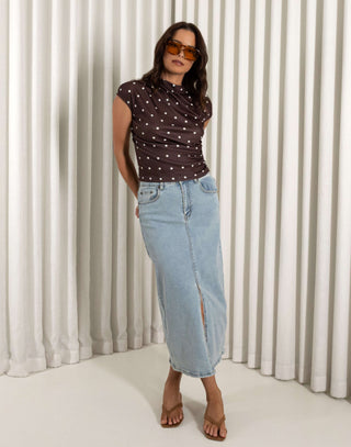 Woman wearing a polka dot top and denim skirt against a white curtain background Light denim high waisted skirt with front split