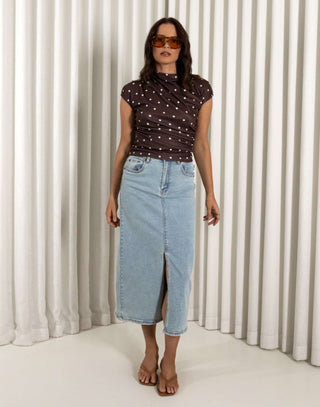 Woman wearing a polka dot top and denim skirt against a white curtain background Light denim high waisted skirt with front split
