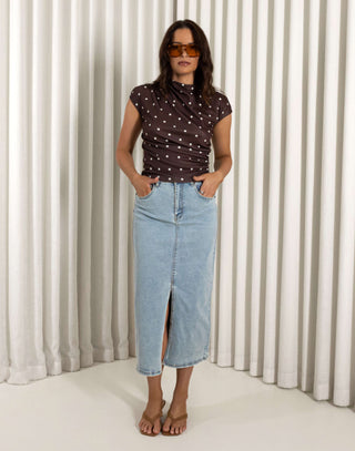 Woman wearing a polka dot top and denim skirt against a white curtain background Light denim high waisted skirt with front split