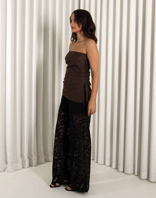 Woman wearing a strapless brown top and black lace pants against a white curtain background Brown strapless top with asymmetrical hem and side split