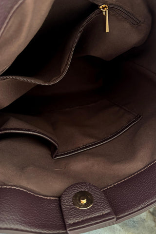Close-up of the interior of a dark brown leather handbag, showing a zippered pocket with a gold zipper pull and a gold snap button closure.