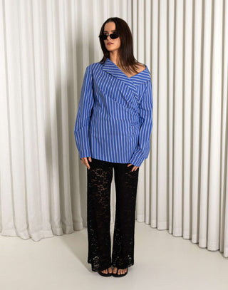 Woman wearing a blue striped shirt and black lace pants against a white curtain background