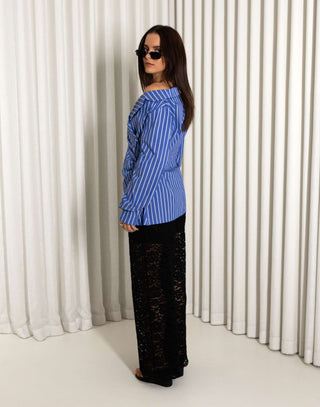 Woman wearing a blue striped shirt and black lace pants against a white curtain background