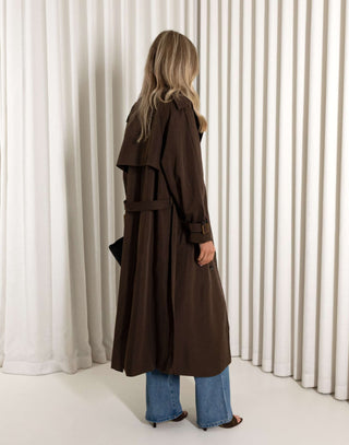 Person wearing a long brown coat standing in front of white curtains