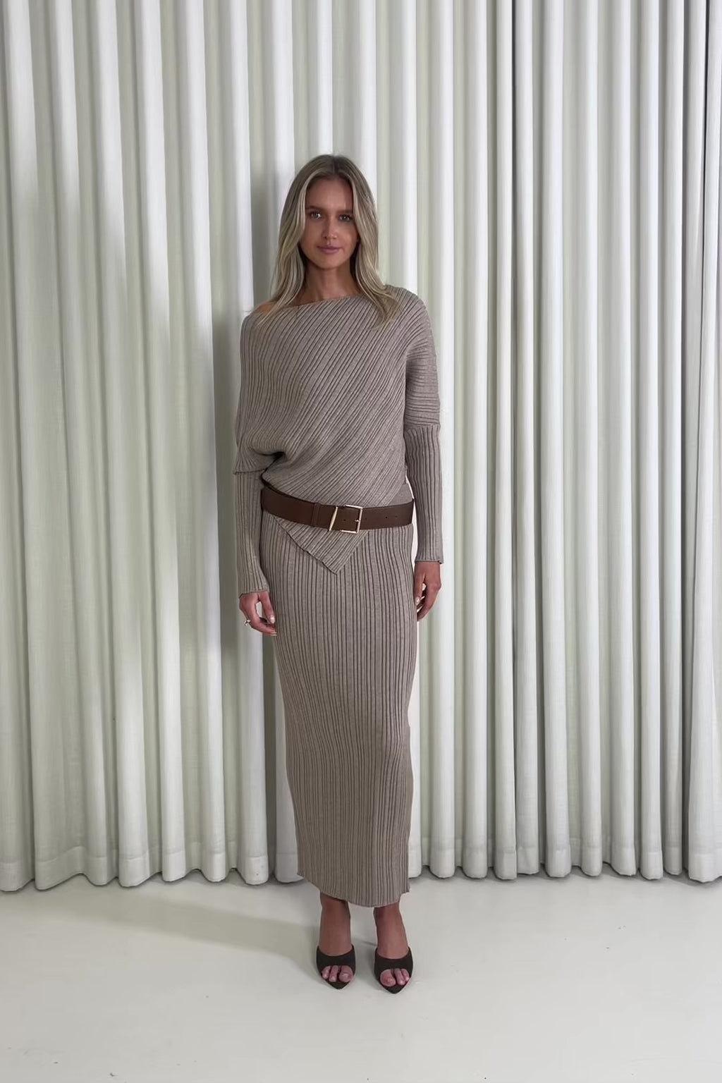 Woman wearing a brown ribbed top and skirt set against a white curtain background