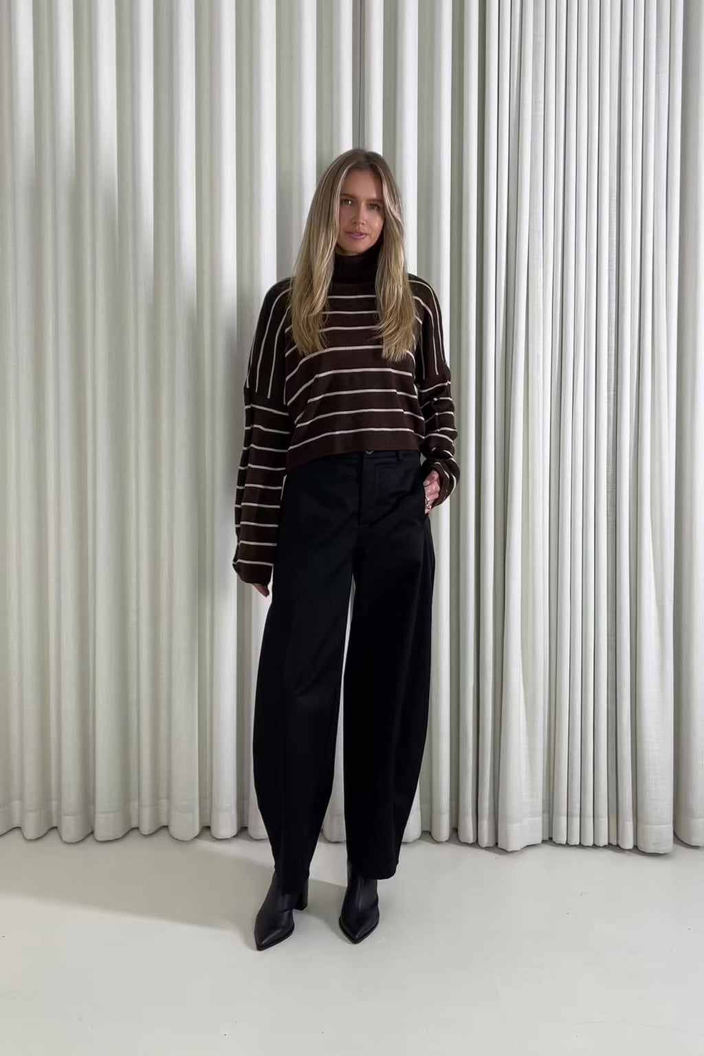 woman wearing a brown and beige striped sweater against a white curtain background