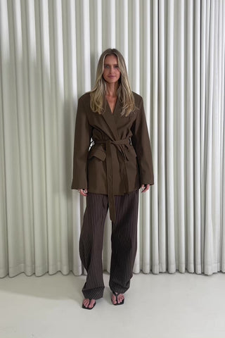 Woman wearing a brown suit standing against a white curtain background