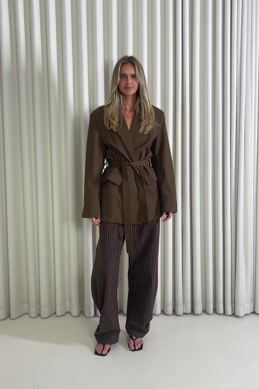 Woman wearing a brown suit standing against a white curtain background