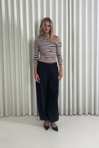 Woman wearing a striped top and black pants standing against a white curtain.