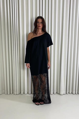 Woman wearing a black one-shoulder dress with lace detailing against a white curtain background Black off shoulder lace maxi dress