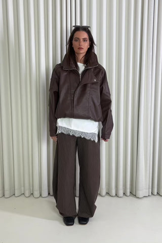 Person wearing a brown outfit with a white lace top against a white curtain background