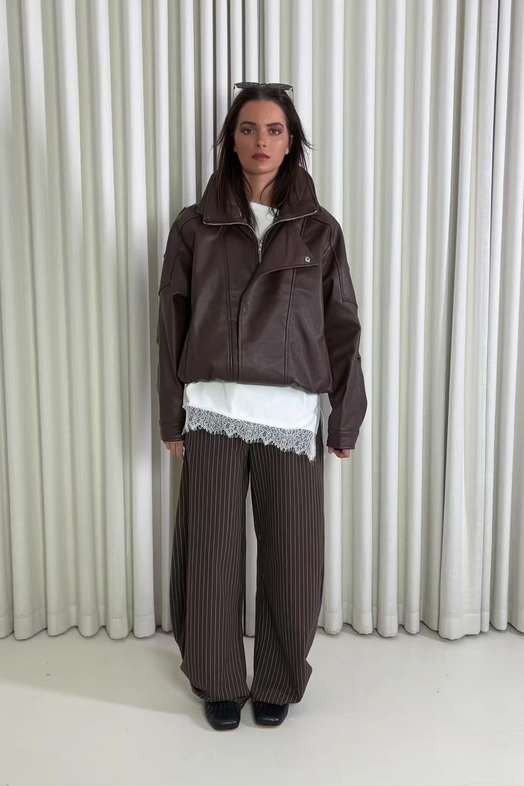 Person wearing a brown outfit with a white lace top against a white curtain background