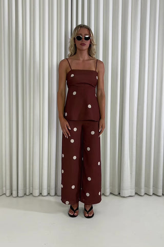 Woman wearing a brown polka dot outfit against a white curtain background Leo brown polka dot tie-back top and wide-leg pants set