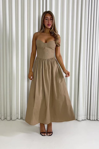 Woman wearing a brown dress standing against a white curtain. Robin mocha fit-and-flare maxi dress with wireless cups
