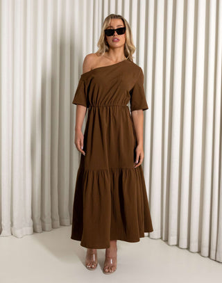 Woman wearing a brown one-shoulder dress against a white curtain background Brown off shoulder midi dress with relaxed tiered shape