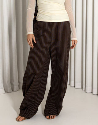 Person wearing brown pinstripe pants against a white curtain background
