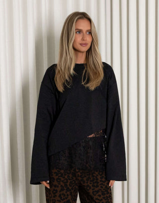 Woman wearing a black lace top and leopard print pants standing against a white curtain.