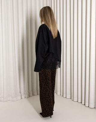 Woman wearing a black lace top and leopard print pants standing against a white curtain.