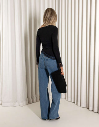 Woman wearing a black top and blue jeans standing in front of white curtains.