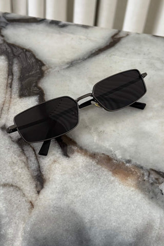 A pair of square-frame sunglasses with dark lenses resting on a white and gray marble surface.