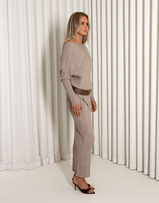 Woman wearing a brown ribbed top and skirt set against a white curtain background