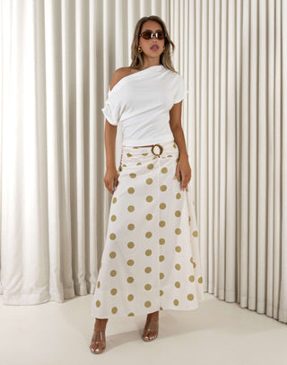 Woman wearing a white off-shoulder top and polka dot skirt against a white curtain background Vanessa cream polka dot maxi skirt with gold waist detail