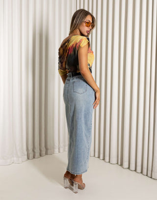 Woman wearing a colorful top and blue jeans standing against a white curtain. Will off shoulder mesh print top, fitted waist
