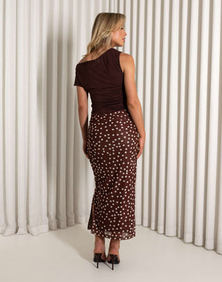 Woman wearing a brown one-shoulder top and polka dot skirt against a white curtain background Brown printed high waisted midi skirt worn by model
